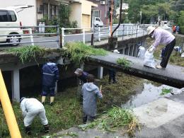 道路わきの小さな川の清掃作業をしている人々の写真