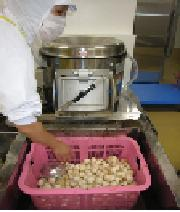 ピーラーで剥かれた野菜をチェックしている給食調理員の様子の写真