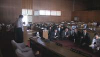 木壁に囲まれた体育館内で避難訓練する議員達の写真
