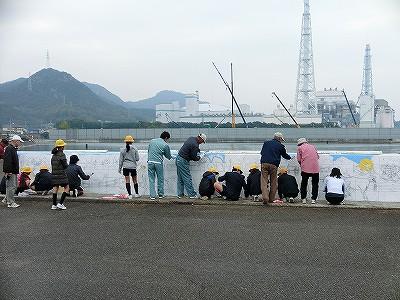 児童と大人たちが護岸の壁に絵を描いている写真