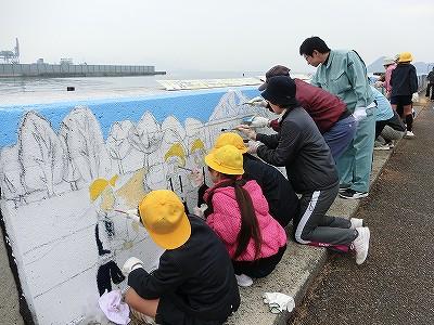 児童たちが護岸の壁に絵を描いている写真