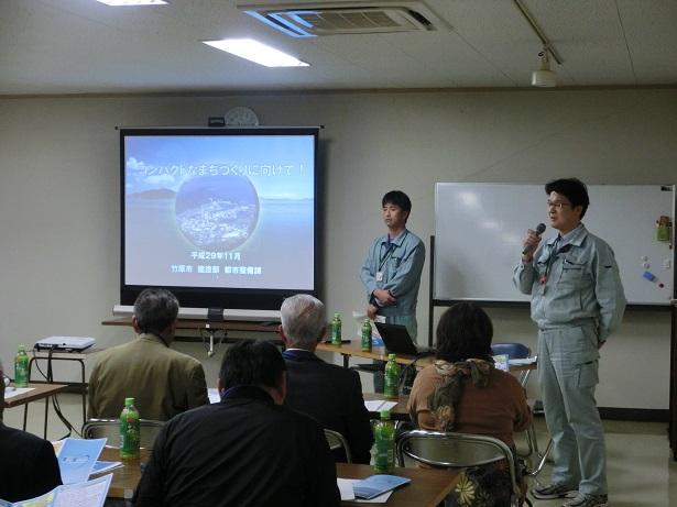 大型テレビを使って説明をしている作業着姿の2人人々の写真