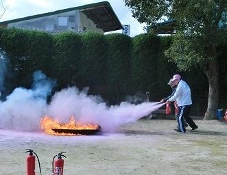消化訓練に参加している人が本物の消火器を使って本物の火を消火している写真