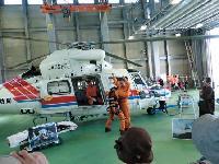 建物の中で停まっているヘリコプターから出てきたオレンジ色のつなぎを着た関係者たちの写真