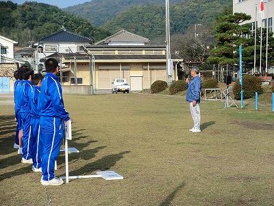 グラウンドで挨拶をしている男性と正面に立つ子供達の写真