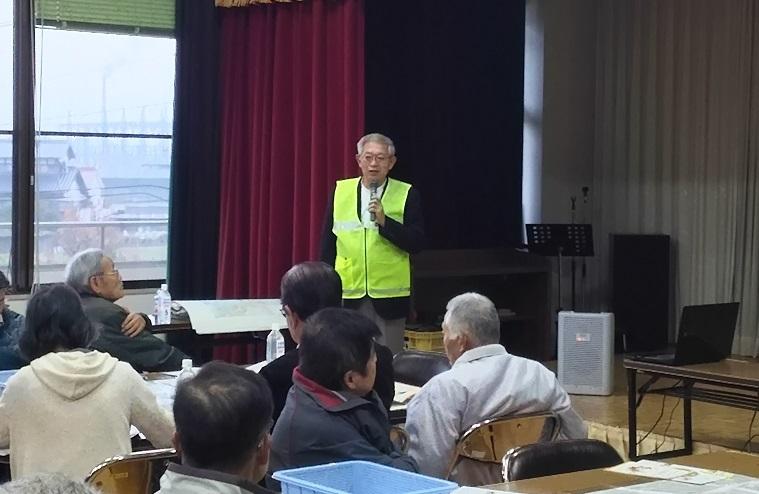 蛍光色のベストを着た防災士がマイクを持って参加者に説明している写真