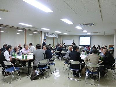 大きな会議室で大勢の人たちがテーブルを囲み談笑している写真