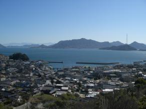 奥に山が見え、中景に水辺が見え、前景に家々が立ち並ぶ街が見える写真