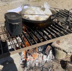 袋に入ったカレーが鍋で茹でられていて隣の飯盒とともに炭火でたかれている写真