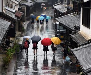 雨が降っている古風な街並みの通りを傘をさして歩いてる人の写真