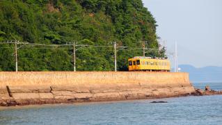 海岸沿いの沿線をオレンジ色の電車が通過中の写真
