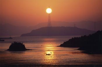 海岸で太陽が丁度鉄塔に重なっている写真