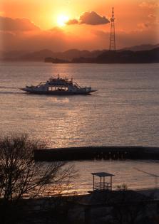 太陽が雲に半分隠れていて、手前を船が渡っている写真