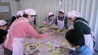 ピンクのエプロンを着た女性たちが食事をしている写真