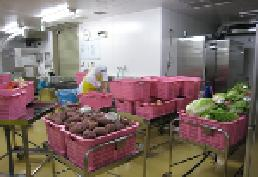 大量のピンクのケースに野菜を入れていく給食調理員の様子の写真