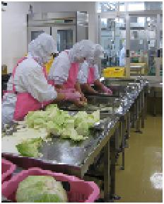 給食調理員3人がかりでシンクで野菜を洗っている様子の写真