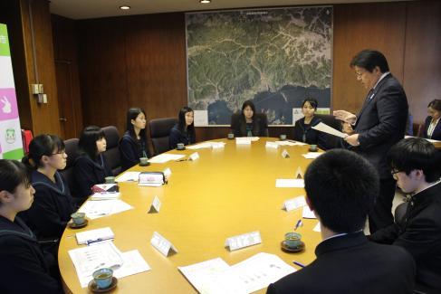 制服を着た男女複数の生徒が机を囲み真剣に話しを聞いている写真